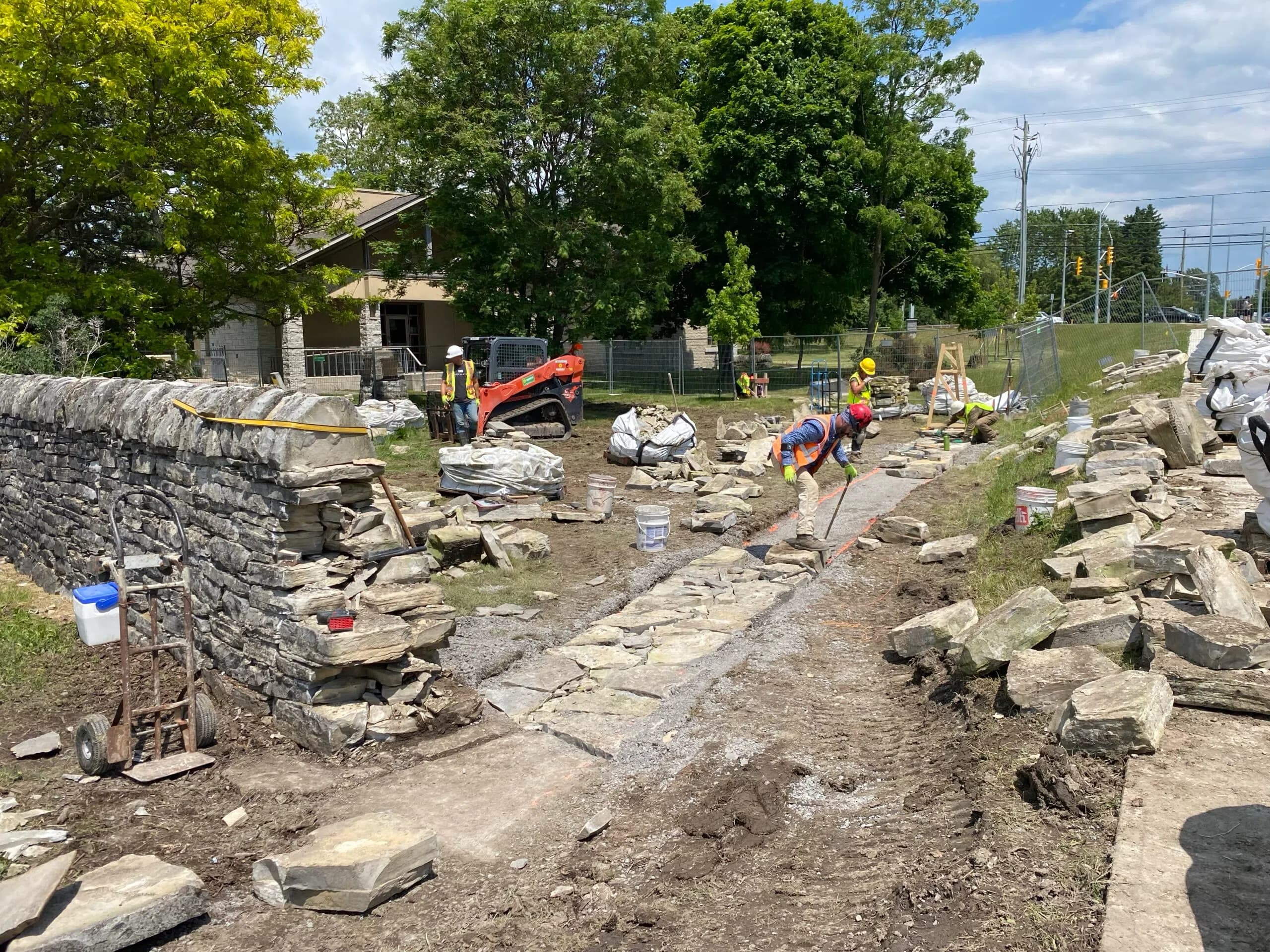 Wallers setting the foundation course for the relocated Kingston wall, with the standing limestone wall to the left and the library's stone house behind.