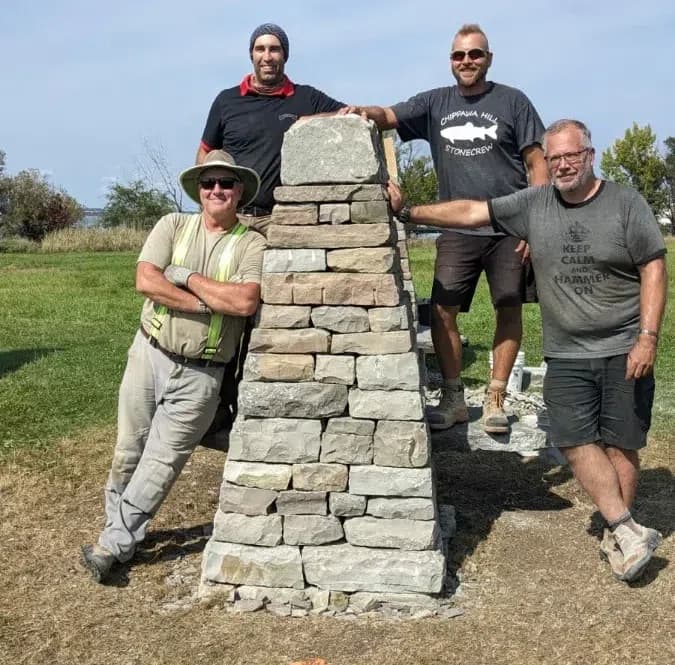 Four wallers standing around the rebuilt coursed pillar at the Amherst Island solar alignment site, its capstone level with their shoulders.