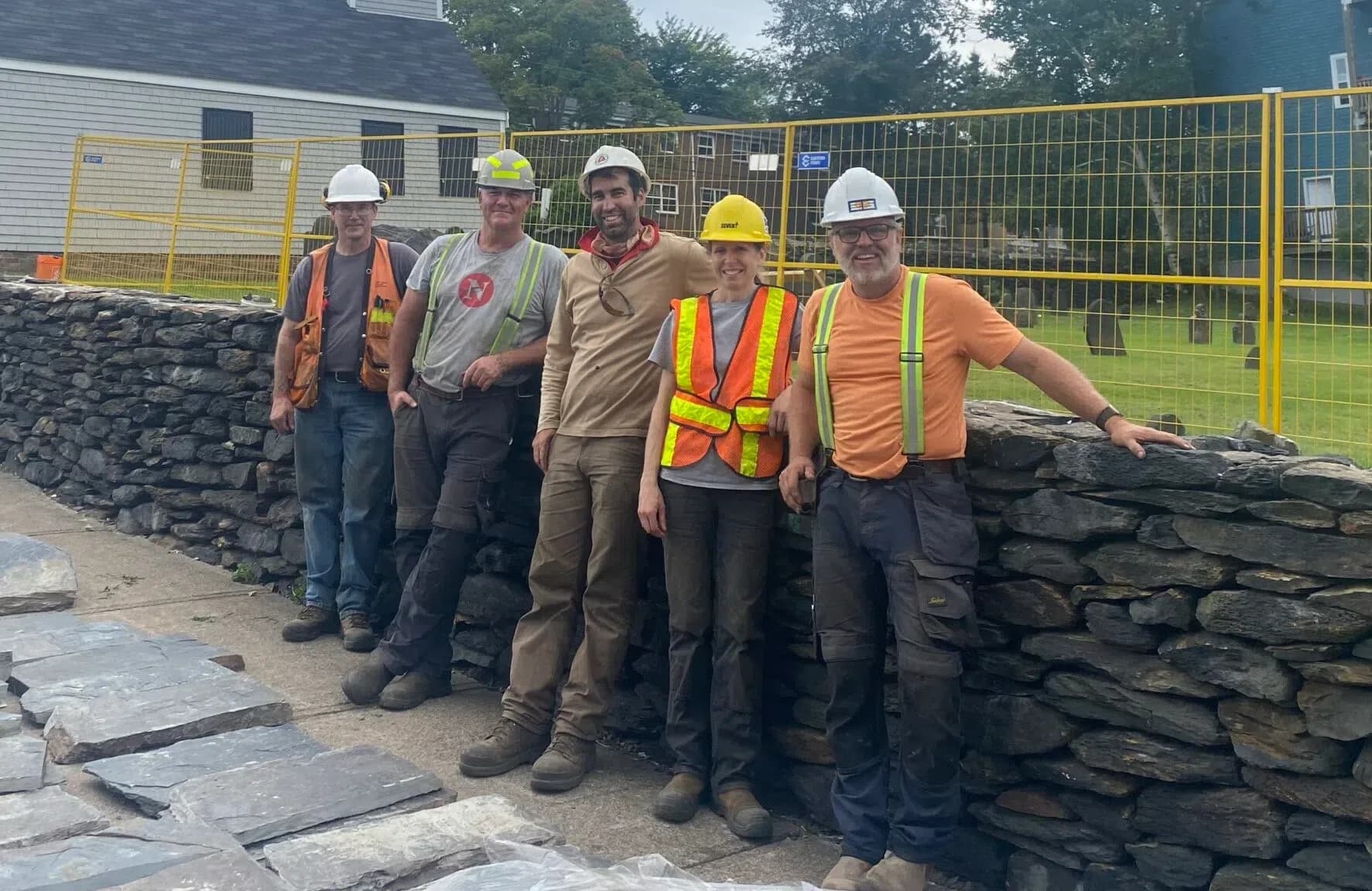 Five members of the co-operative in hard hats and hi-vis, standing along a rebuilt dry stone wall on site.
